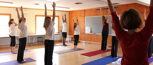 Class members reaching arms overhead together in a sunlit studio