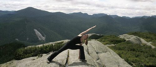 Becky Bell holding extended side-angle pose on a mountain summit overlooking a forested valley