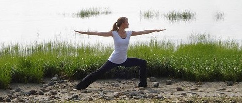 Becky Bell holding warrior II pose beside a marsh at golden hour
